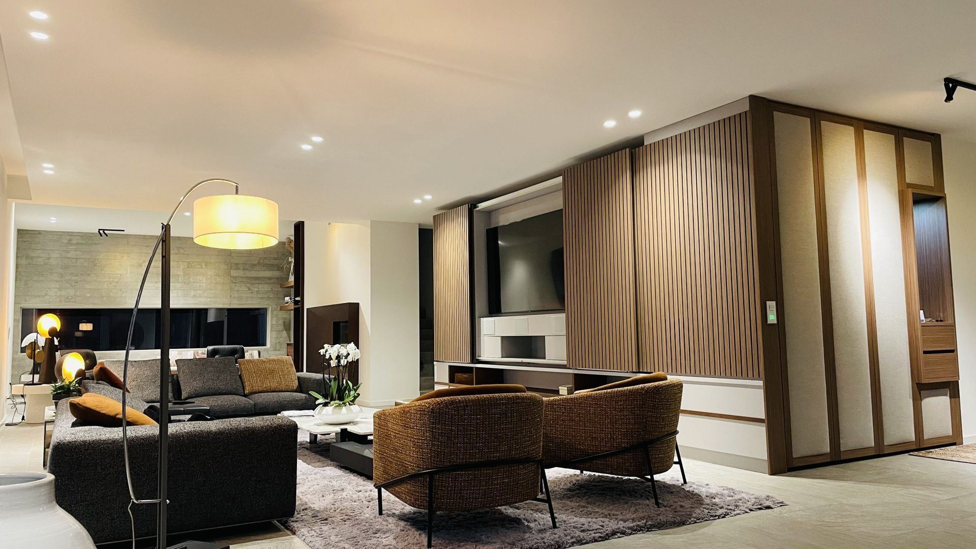 Un salon moderne avec des fauteuils à motifs, un tapis moelleux, une lampe d'angle et un meuble TV intégré.