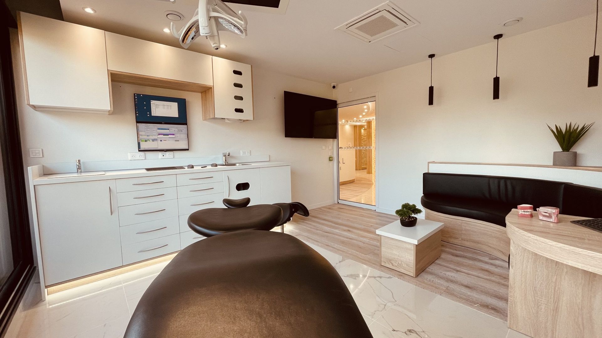 Une salle de soins médicaux ou esthétiques lumineuse et moderne, avec des meubles blancs, une table d'examen noire et une salle d'attente.