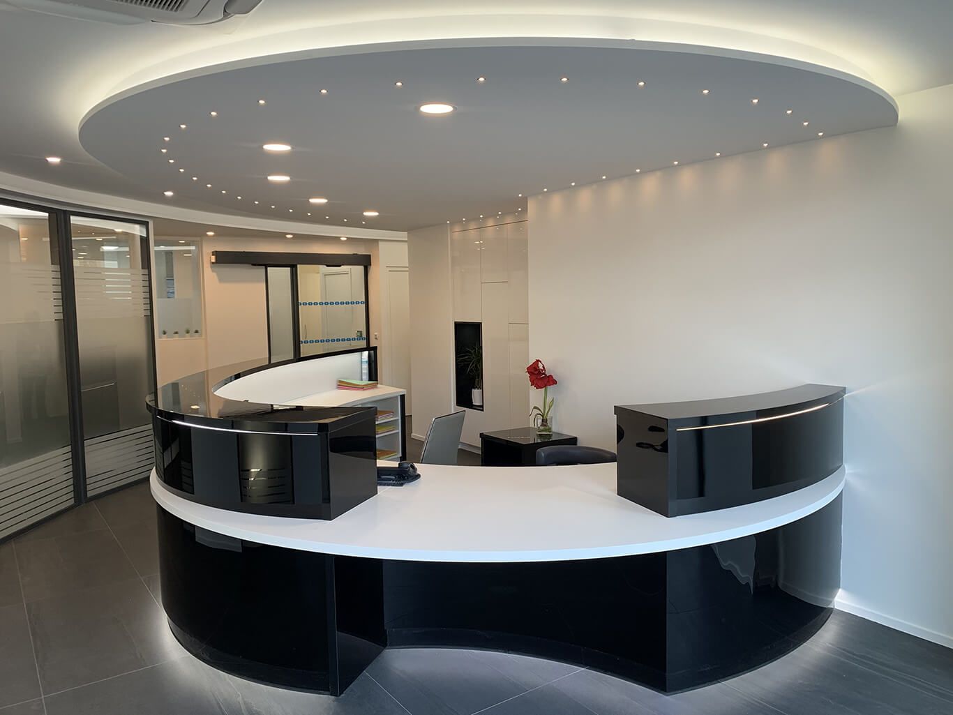 Comptoir d'accueil moderne avec un plateau blanc et un piètement noir brillant, sous un plafond circulaire encastré avec éclairage LED.