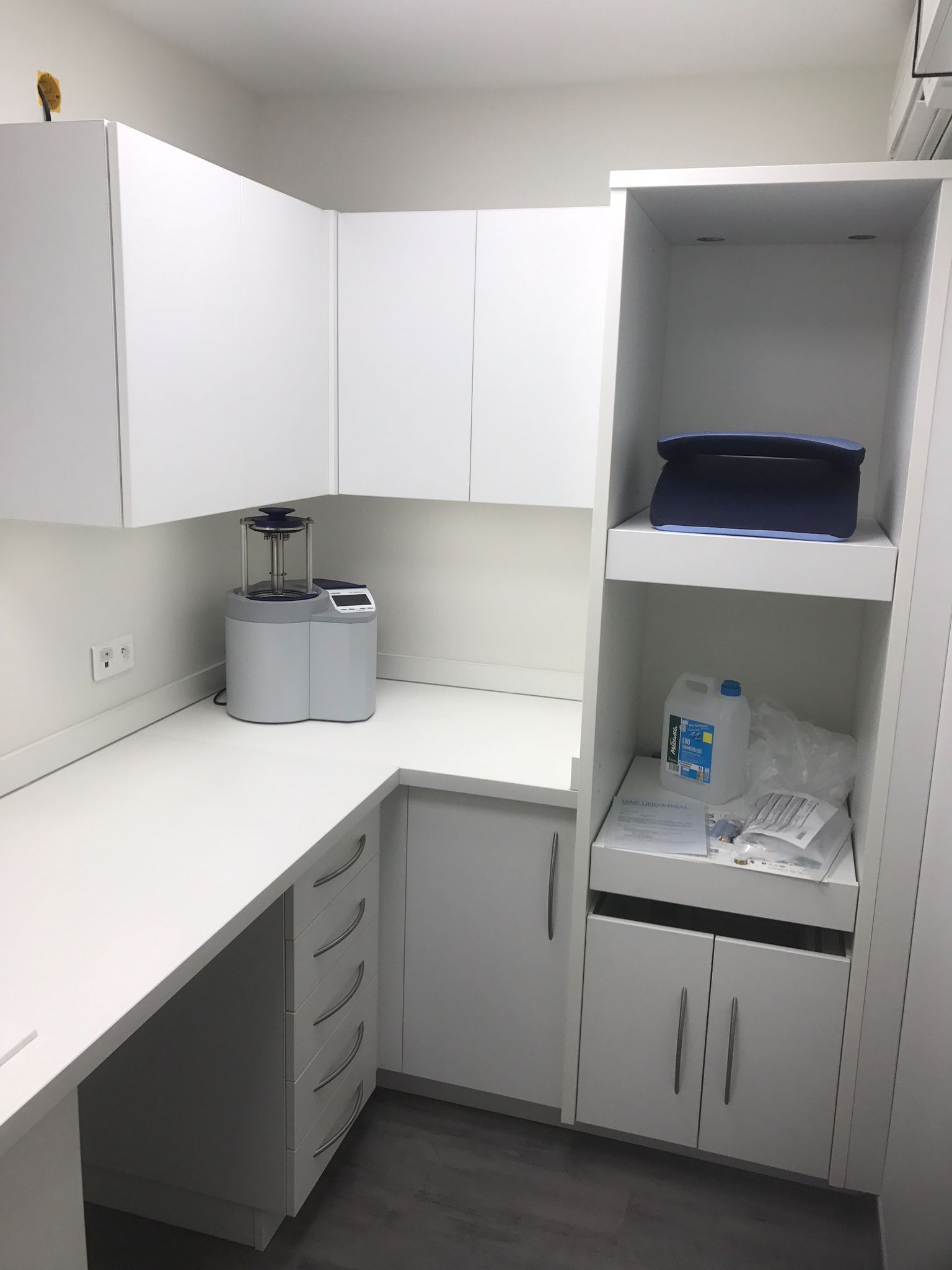 Un poste de travail de laboratoire blanc et épuré, comprenant des armoires d'angle, un appareil central, des tiroirs et des étagères ouvertes avec des fournitures.