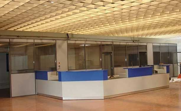Un espace de bureaux intérieur comprenant un long comptoir d'accueil avec des panneaux bleus et blancs sous un plafond suspendu à motif quadrillé.
