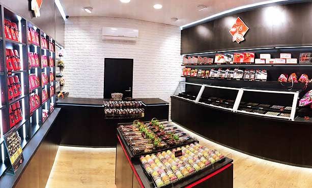 L'intérieur moderne de ce magasin présente des présentoirs de produits rouges sur les étagères, un îlot central et un comptoir de caisse noir.
