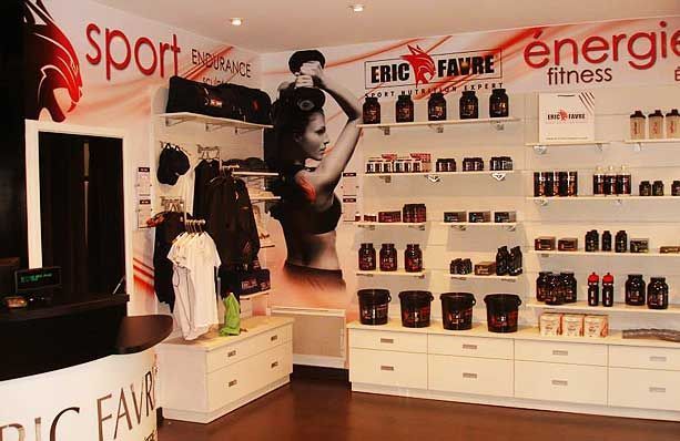 Une boutique de nutrition sportive Eric Favre avec des étagères blanches présentant des flacons de compléments alimentaires et des vêtements exposés.