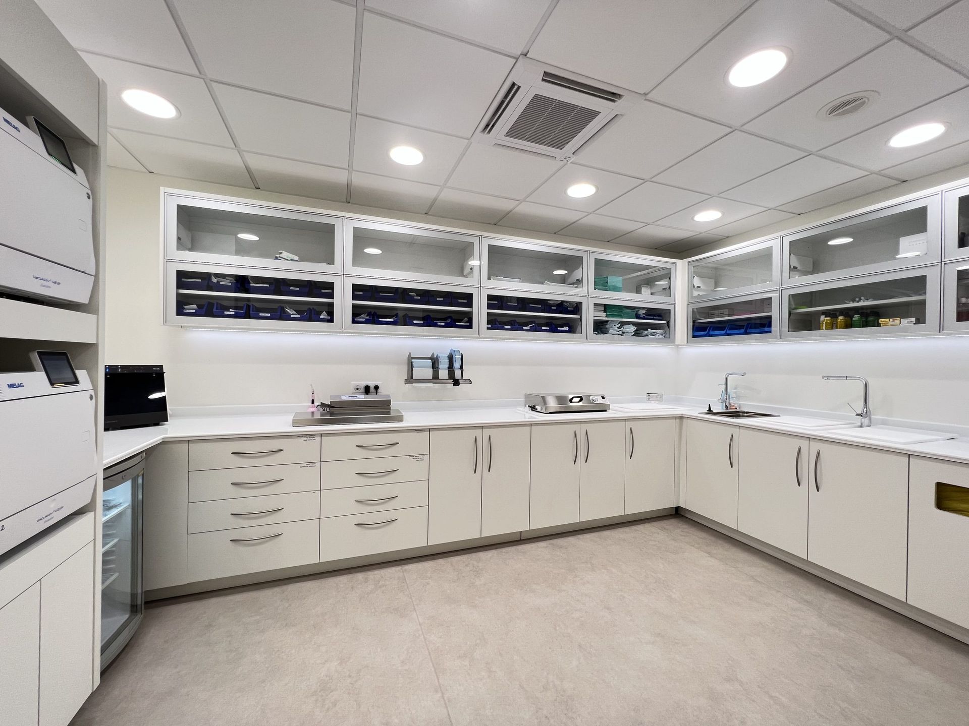 Un laboratoire dentaire stérile avec des armoires blanches, des rangements muraux vitrés, des comptoirs modernes et un éclairage lumineux.