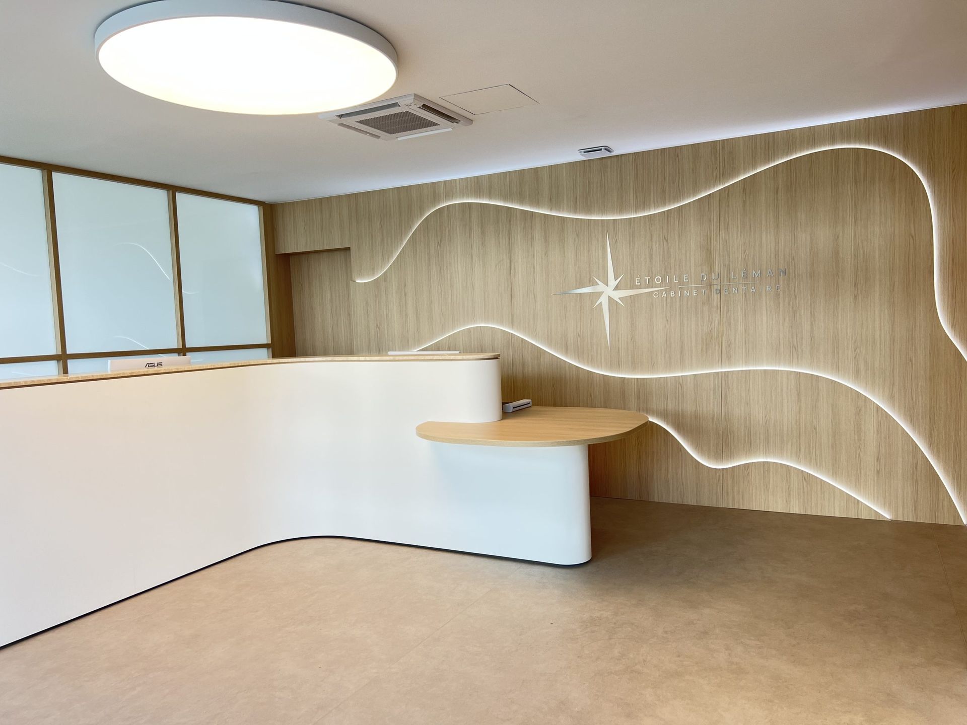 Un espace d'accueil moderne avec un bureau blanc incurvé, des murs lambrissés de bois clair avec un éclairage LED ondulé et une moquette beige.