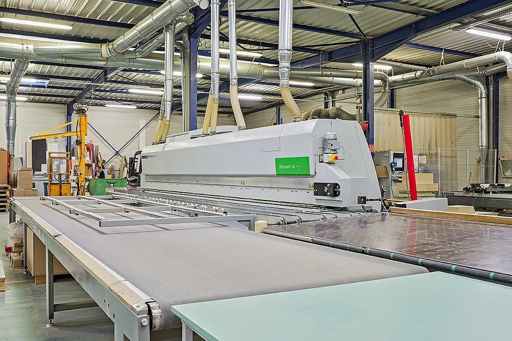 Une grande machine de découpe de métaux industrielle à commande numérique (CNC) fonctionnant sur le sol d'une usine, avec des tuyaux d'aspiration de poussière suspendus.
