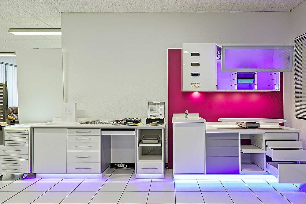 Meubles de laboratoire dentaire modernes avec surfaces blanches, éclairage d'ambiance violet et tiroirs de rangement intégrés.