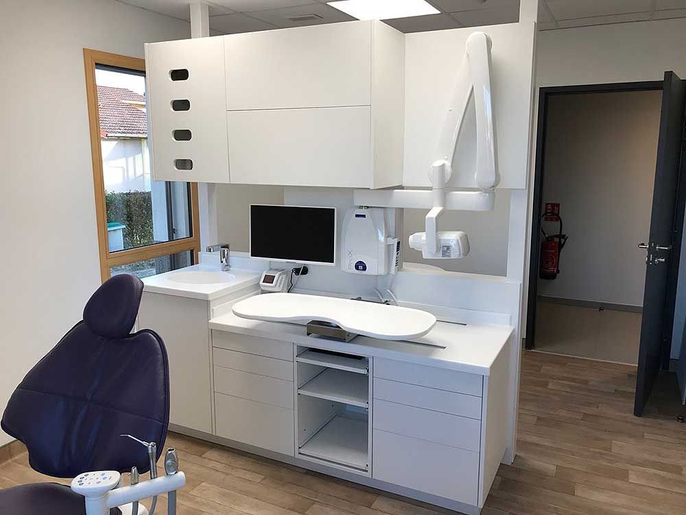 Une salle de soins dentaires avec un fauteuil violet, des meubles blancs, un écran d'ordinateur et du matériel dentaire intégré.