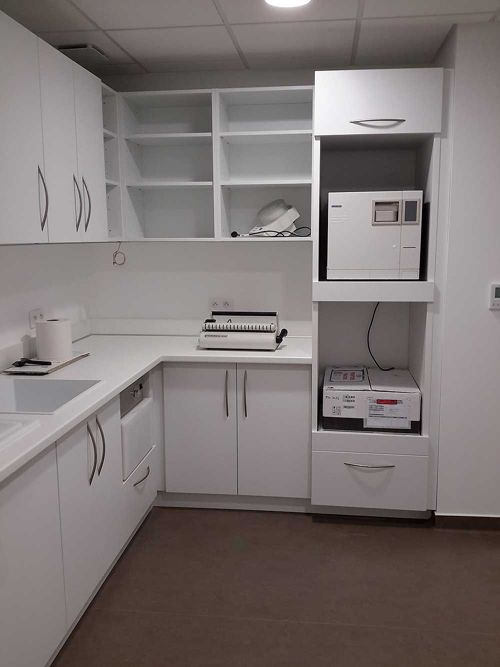 Zone de stérilisation dans une clinique dentaire comprenant des armoires blanches, des comptoirs et du matériel médical.
