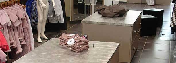 Intérieur d'un magasin de vêtements présentant un mannequin vêtu de rose, des portants de vêtements suspendus et deux tables d'exposition beiges.