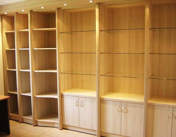 Étagère en bois clair avec étagères ouvertes, étagères vitrées et placards bas, éclairée par des spots.