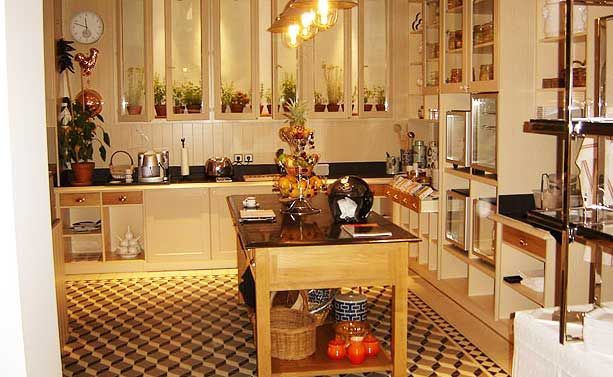 Une cuisine moderne et lumineuse avec un îlot central foncé, des meubles en bois clair, des étagères ouvertes et un sol carrelé à motifs.