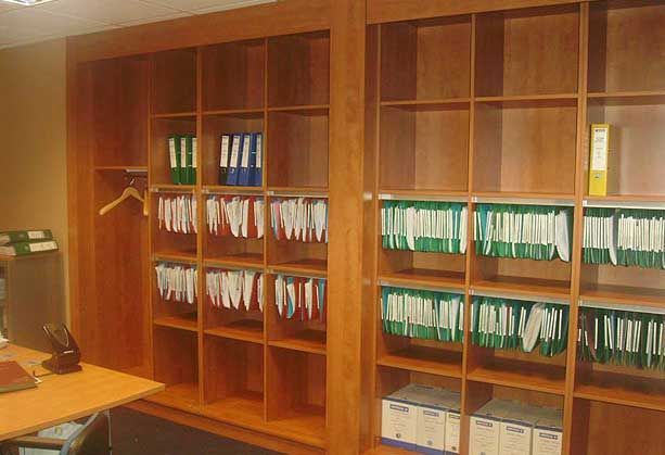 De grandes étagères de bureau en bois remplies de dossiers suspendus, de classeurs organisés et de boîtes de rangement.