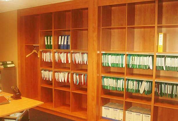 Dans un bureau, un mur d'étagères en bois est rempli de rangées de dossiers suspendus, de classeurs et de boîtes de rangement.