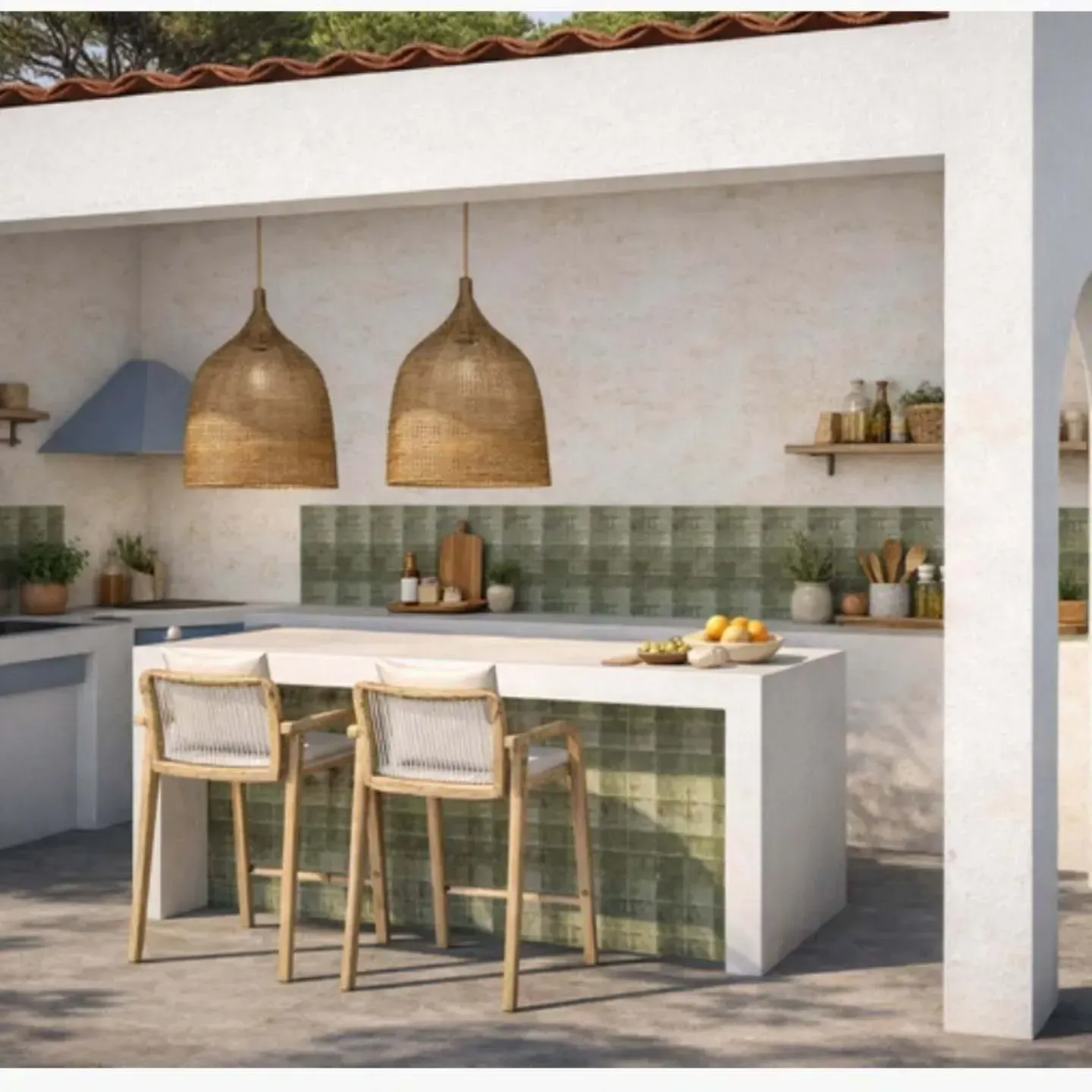 Una cocina exterior de estilo mediterráneo con una isla de piedra, dos lámparas colgantes de ratán y paredes revestidas de azulejos de color verde salvia.