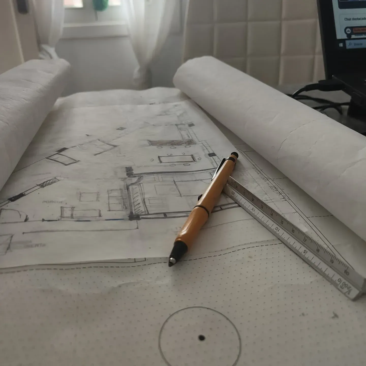 Un portaminas naranja y una regla metálica descansan sobre un dibujo de un plano arquitectónico que hay sobre un escritorio.