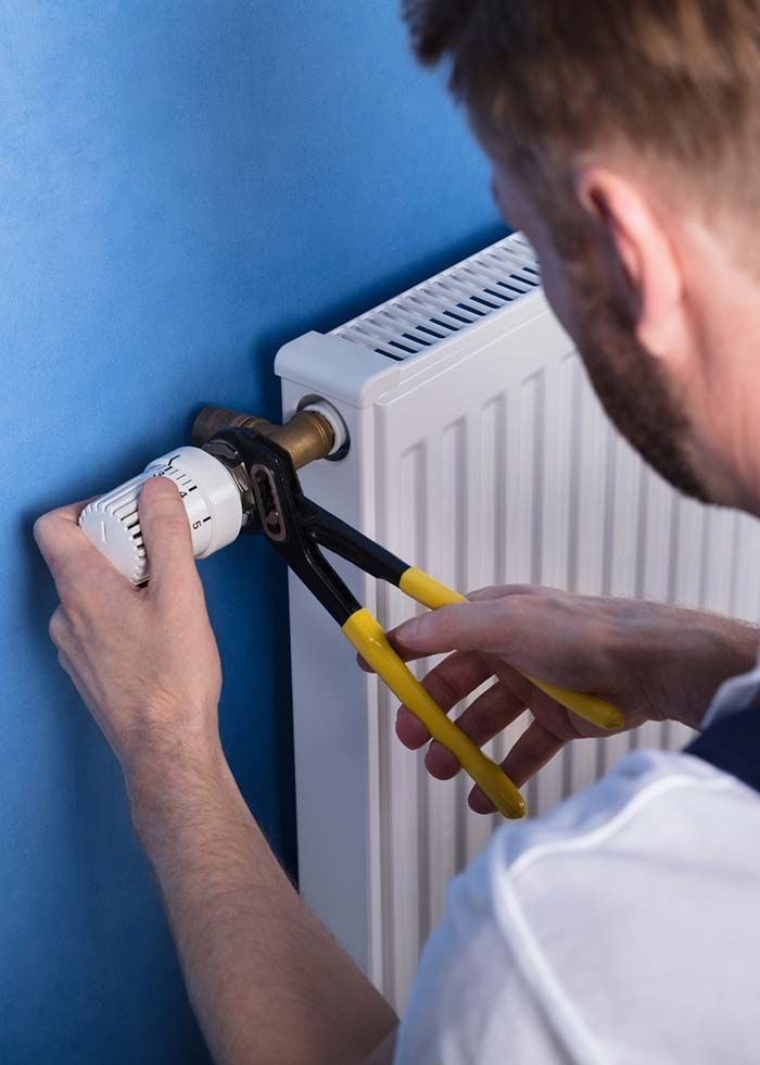 Un hombre está arreglando un radiador con unos alicates.