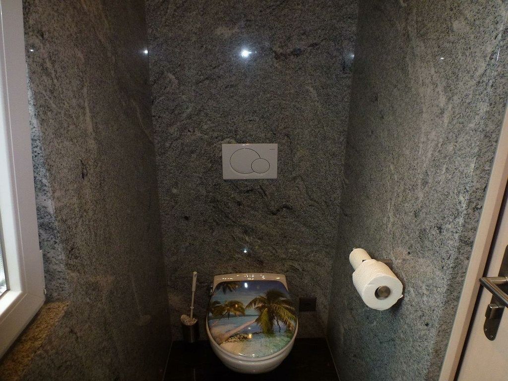 Ein Badezimmer mit Toilette und Papierhandtuchhalter. Steinwand von der Hutter Natursteine AG