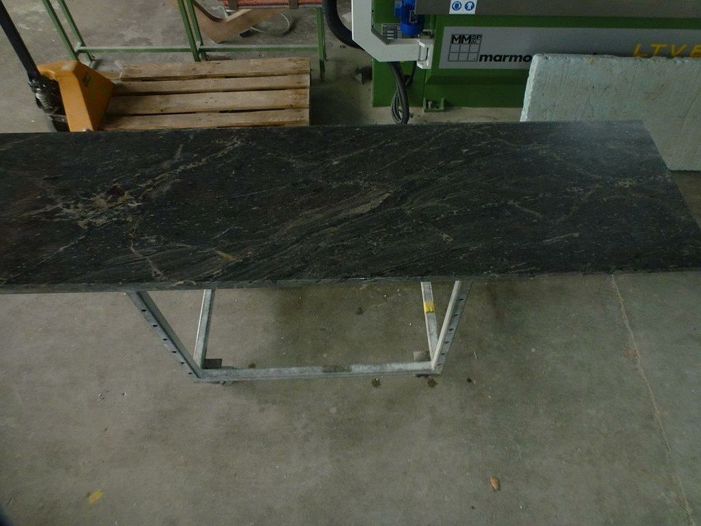 Ein schwarzer Tisch mit Metallgestell und einer Maschine im Hintergrund. Foto von der Hutter Natursteine AG