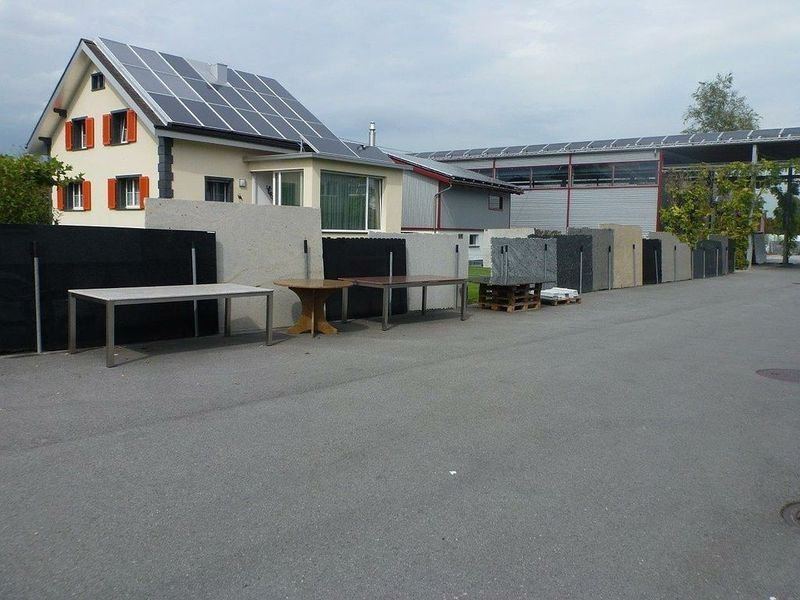 Eine Reihe von Tischen vor einem Haus mit Solarzellen auf dem Dach. Foto von der Hutter Natursteine AG