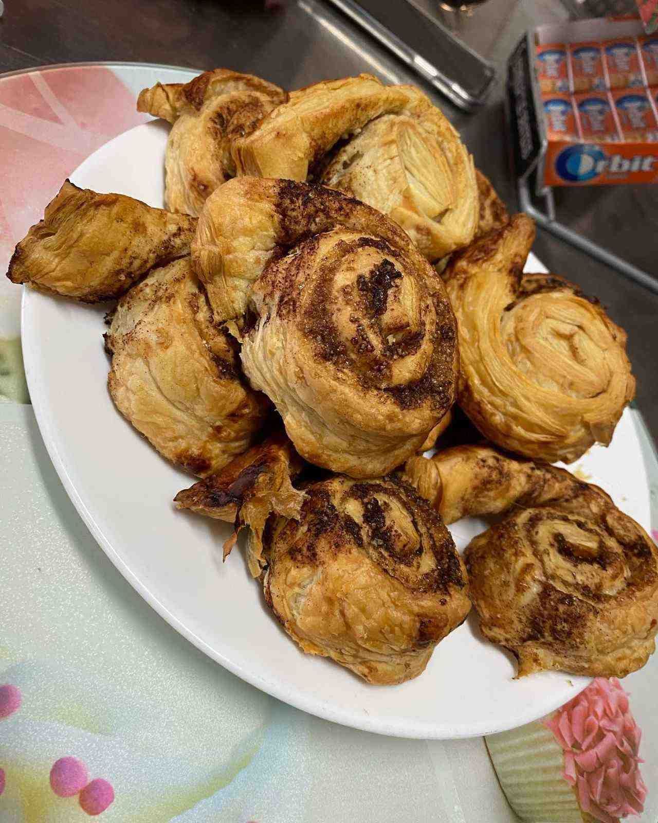 Plato de pasteles en espiral de color marrón dorado sobre una mesa, con una bolsa de aperitivos al fondo.