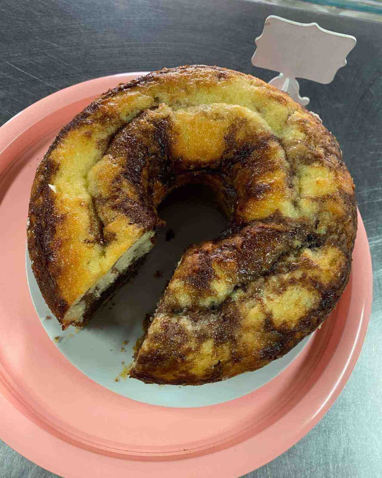 Pastel de canela en un plato rosa, con una rebanada cortada.