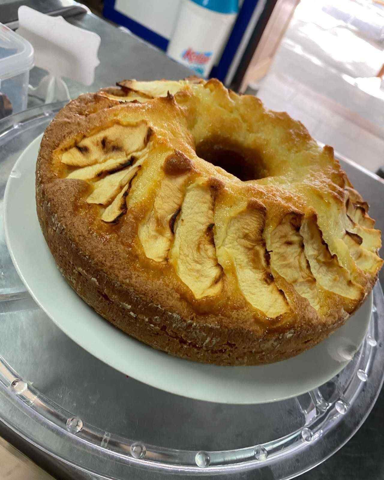 Pastel de manzana tipo bundt en un plato, cubierto con rodajas de manzana, sobre una mesa.