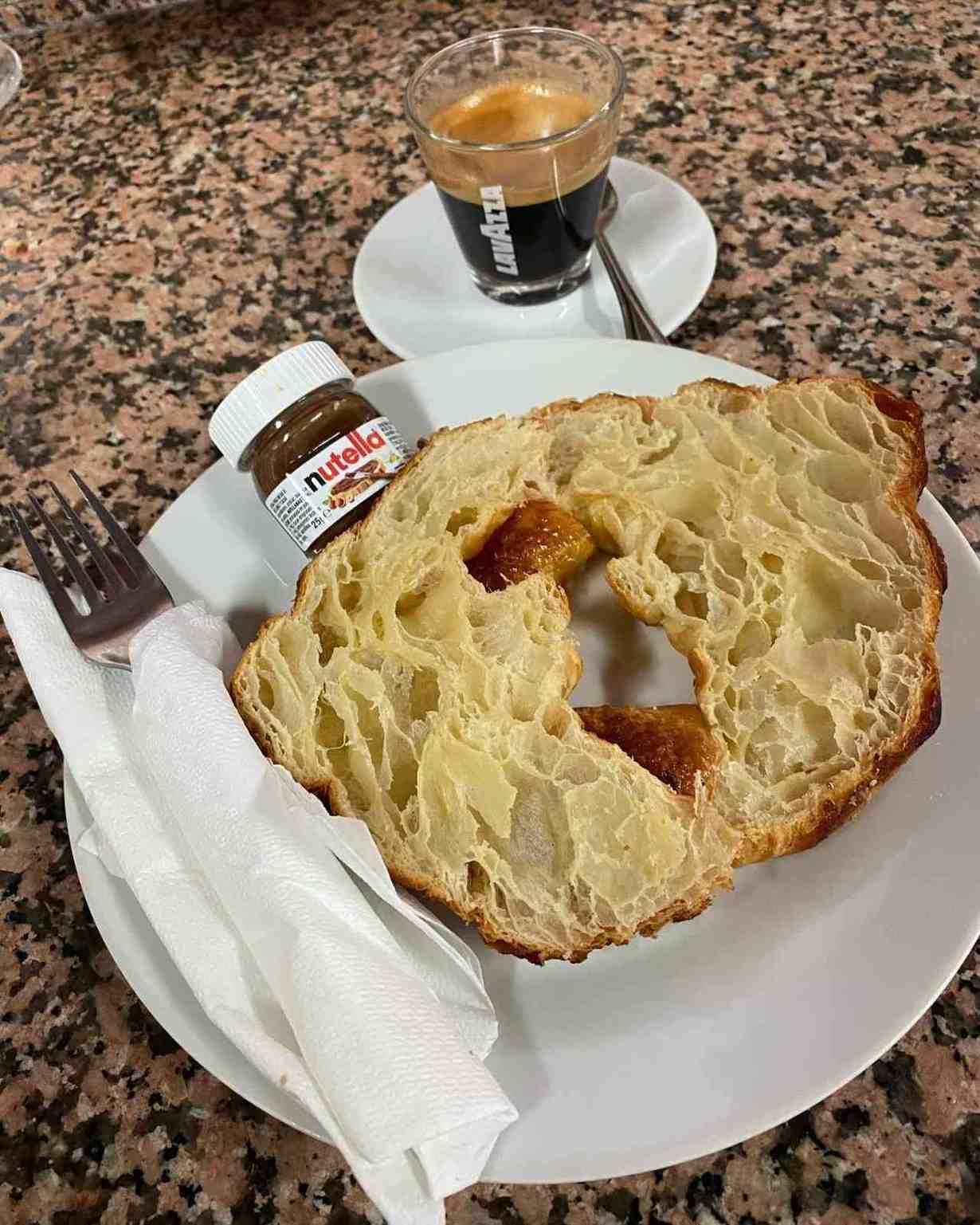 Plato con rebanadas de pan, tarro de mermelada y café expreso sobre una mesa moteada.