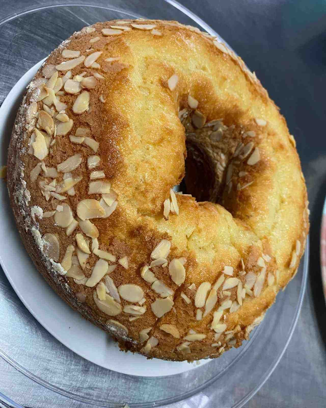 Pastel en forma de anillo con cobertura de almendras doradas, servido en un plato, con centro hueco y corteza dorada.
