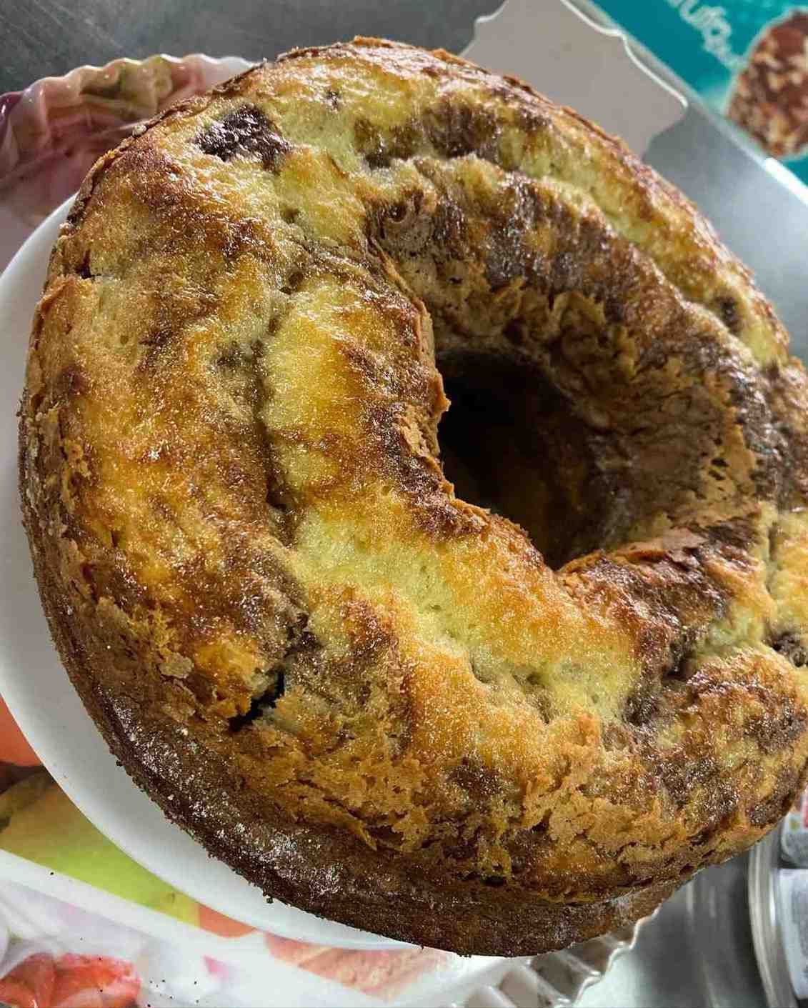 Pastelito en forma de anillo de color marrón dorado con una superficie rugosa y glaseada sobre un plato.