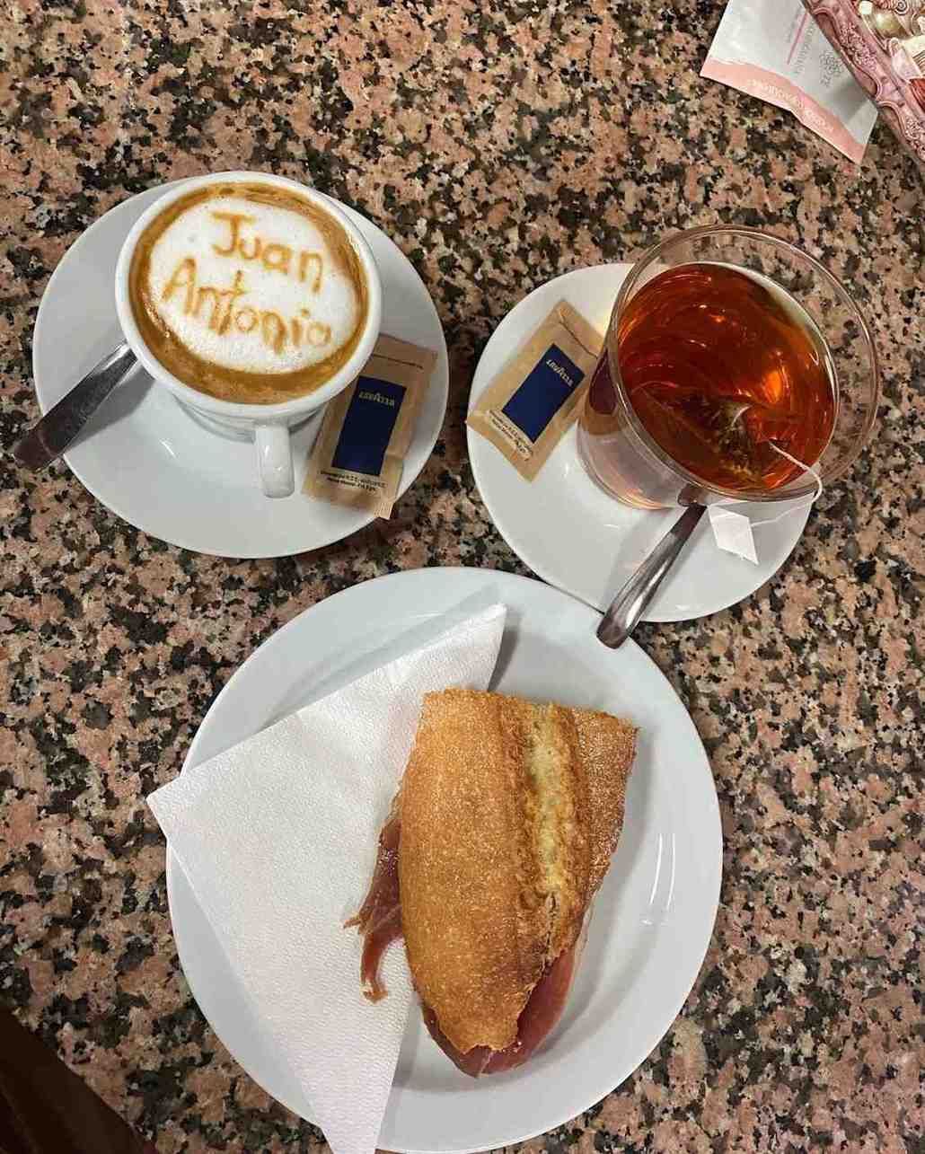 Café y té con sobres de azúcar junto a un sándwich tostado sobre una mesa de granito.