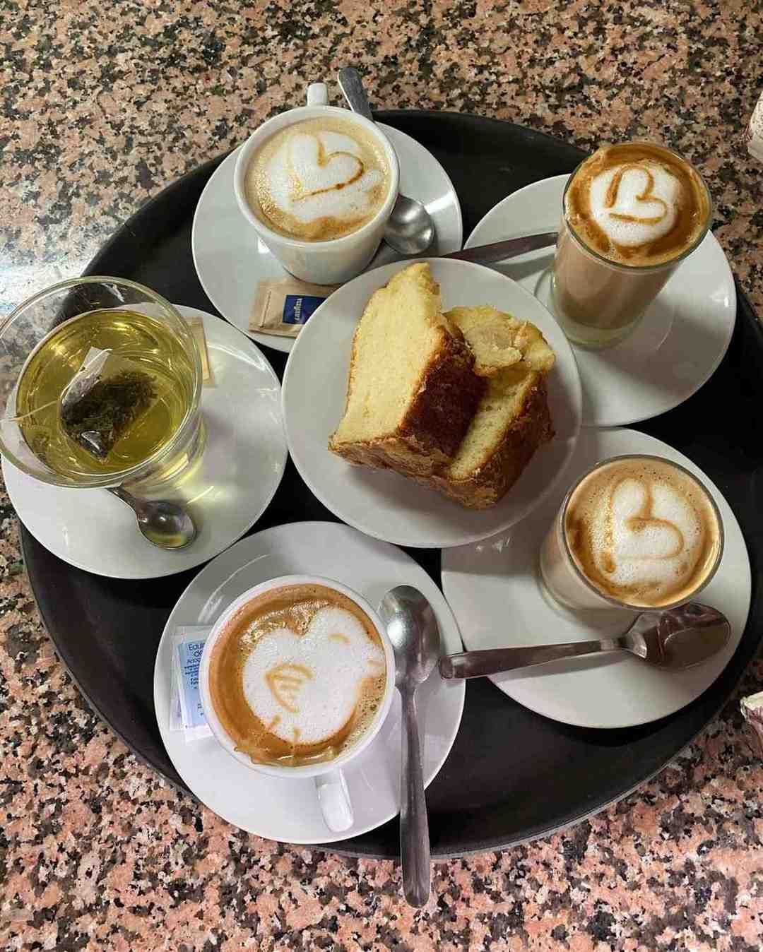 Bebidas de café y pastel en una bandeja, que incluye lattes, una bebida helada y bizcocho en rebanadas.