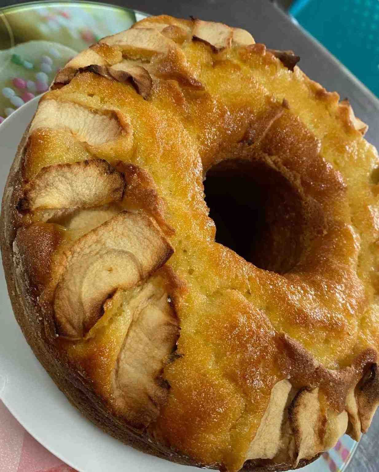 Anillo de hojaldre glaseado cubierto con rodajas de manzana en un plato.