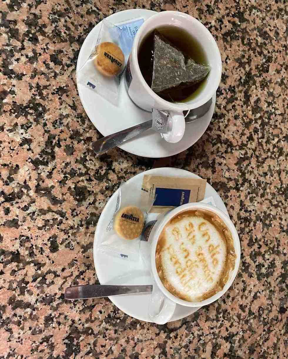 Dos tazas de café con sus platillos, cucharas y galletas sobre una mesa de café moteada.