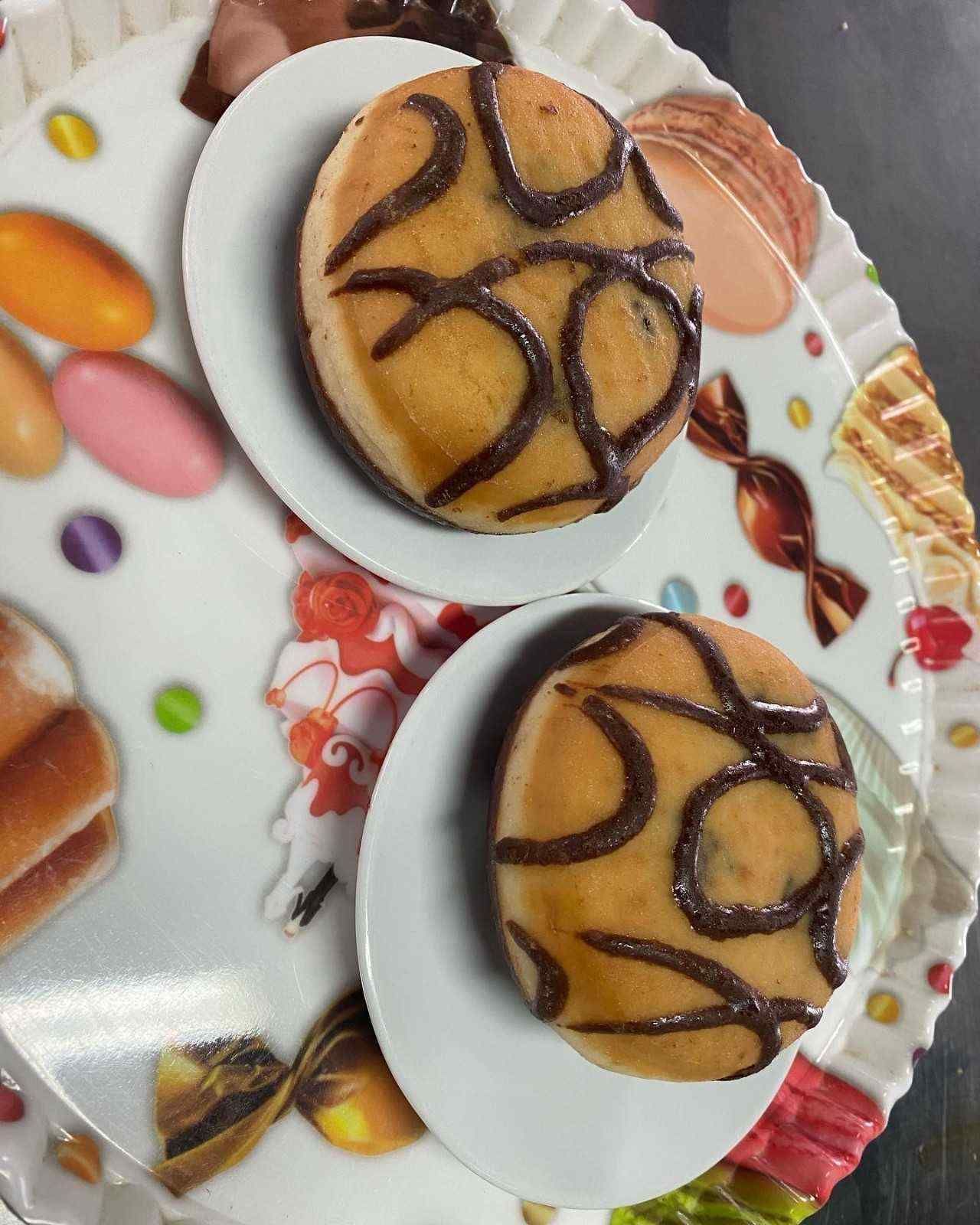 Dos pasteles glaseados con sirope de chocolate sobre platos blancos encima de una bandeja decorativa con motivos florales.