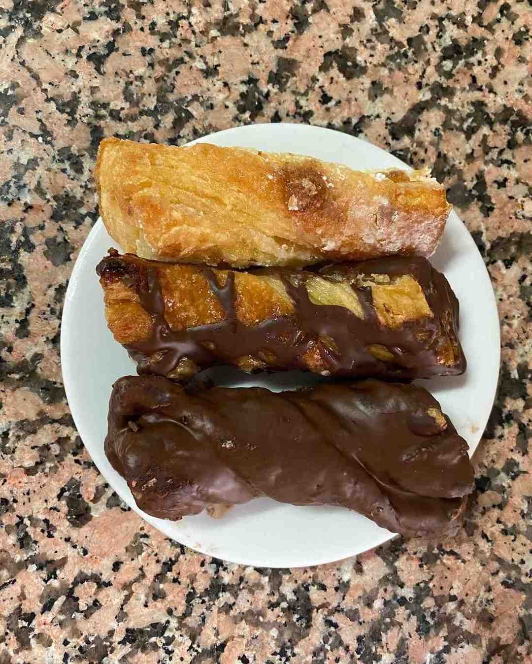 Tres pasteles cubiertos de chocolate sobre un pequeño plato blanco encima de una encimera moteada.