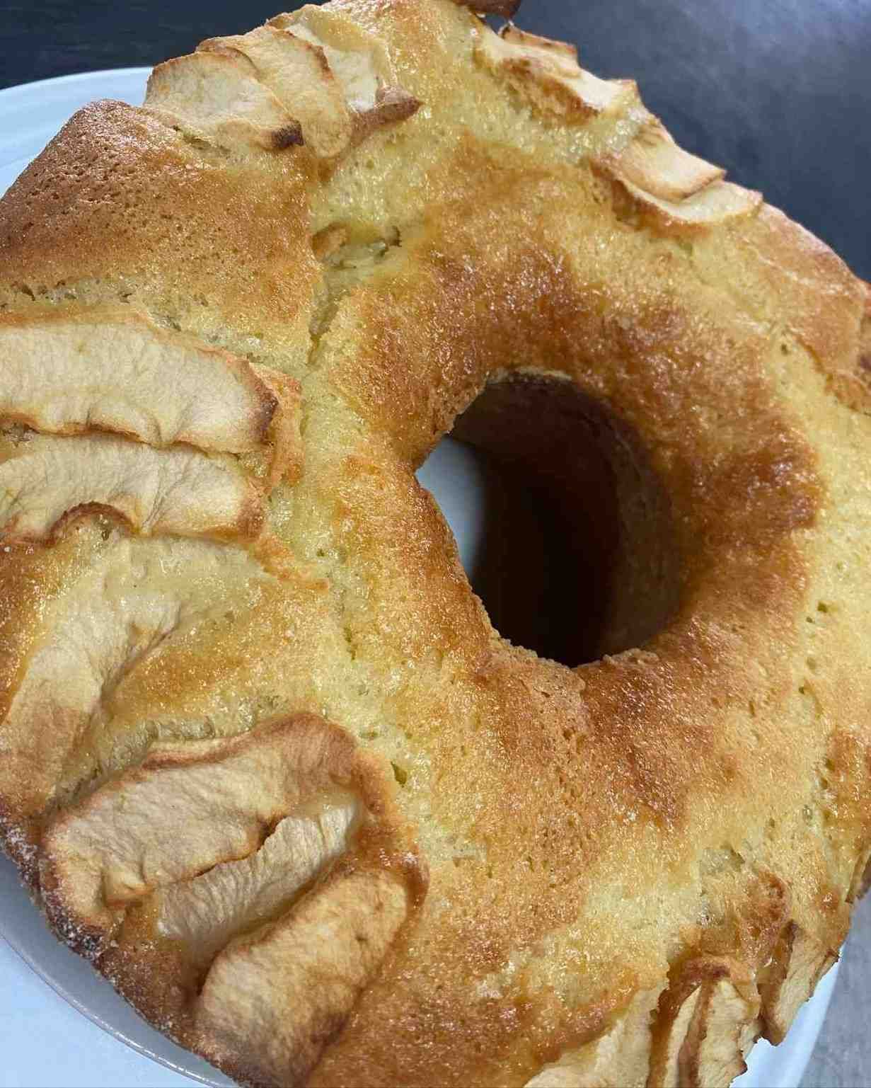 Pan azucarado en forma de anillo con rodajas de manzana horneada encima, sobre un plato blanco.
