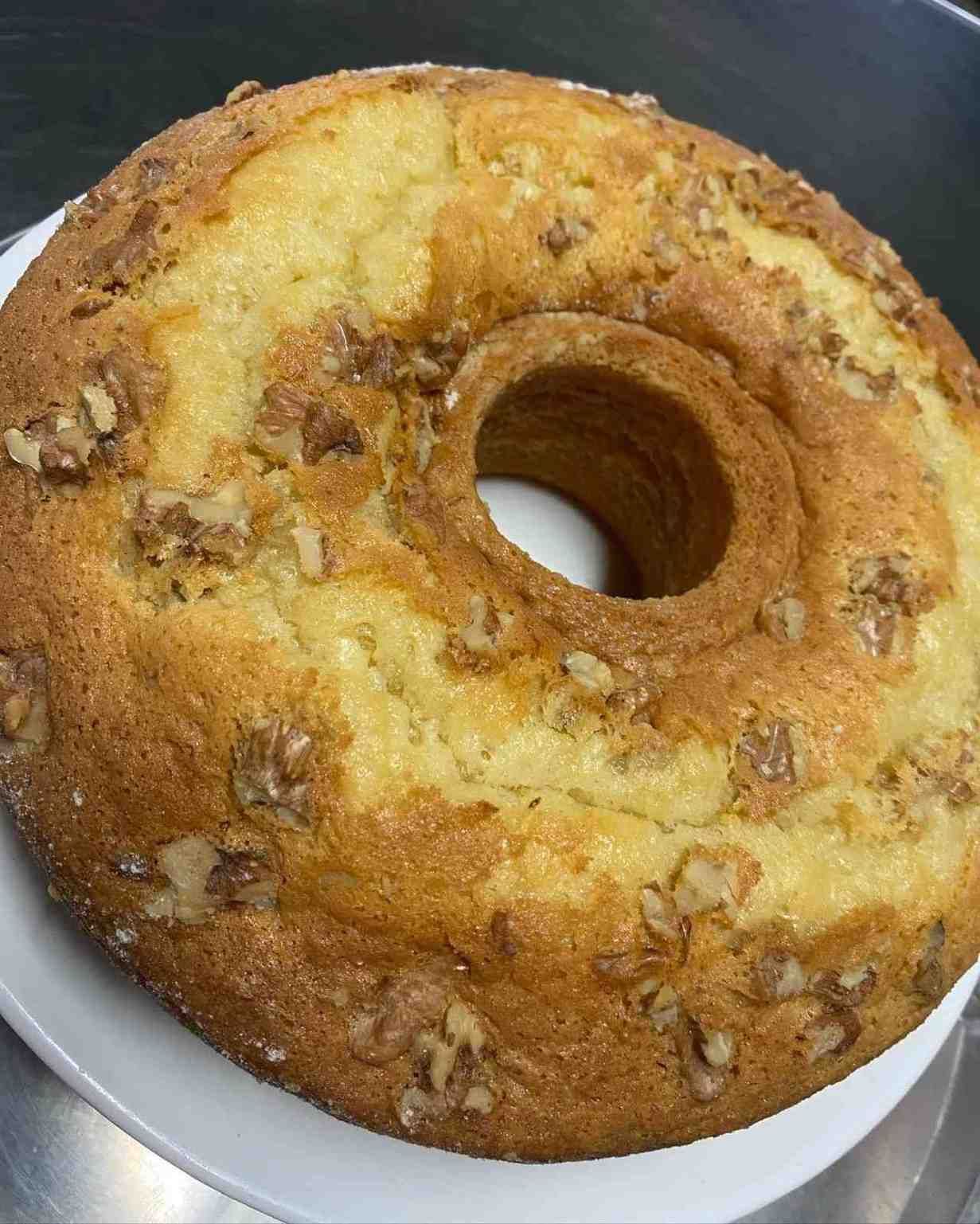 Pastel bundt dorado con nueces picadas encima, servido en un molde redondo.