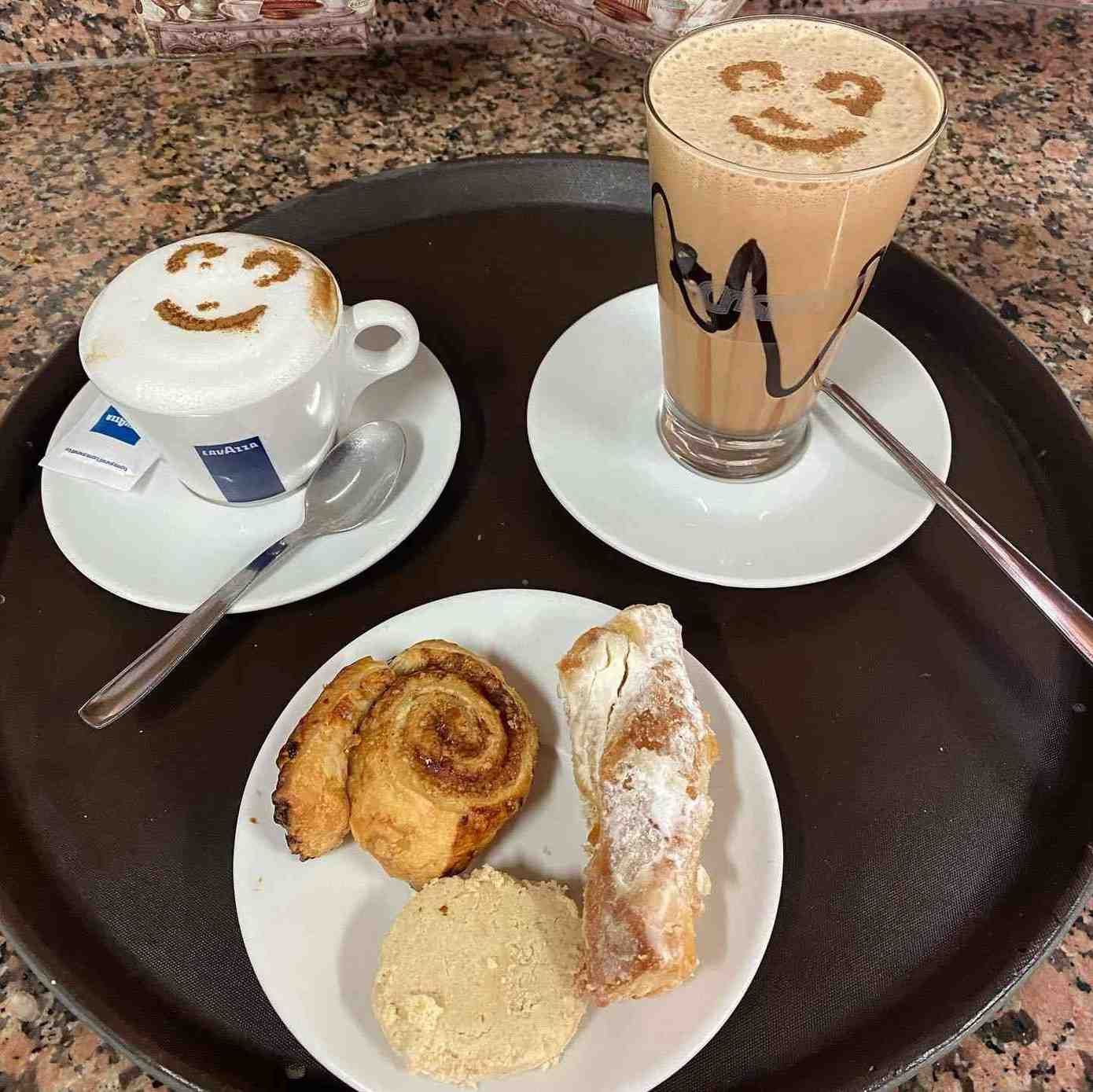 Bandeja de café y postres con capuchino, bebida helada y pasteles sobre una mesa.