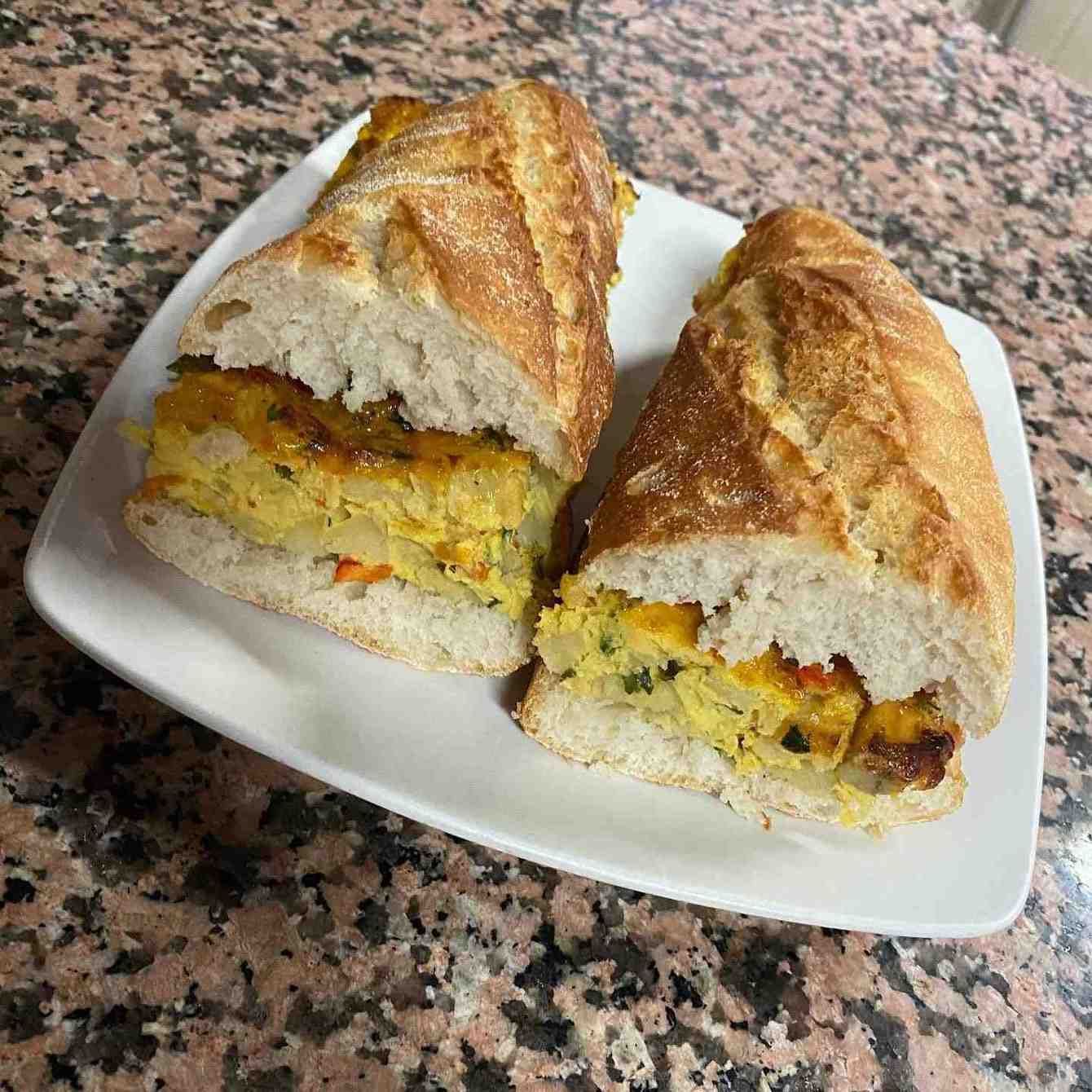 Cortar las mitades del sándwich con relleno de huevo en un plato blanco sobre una encimera de granito.