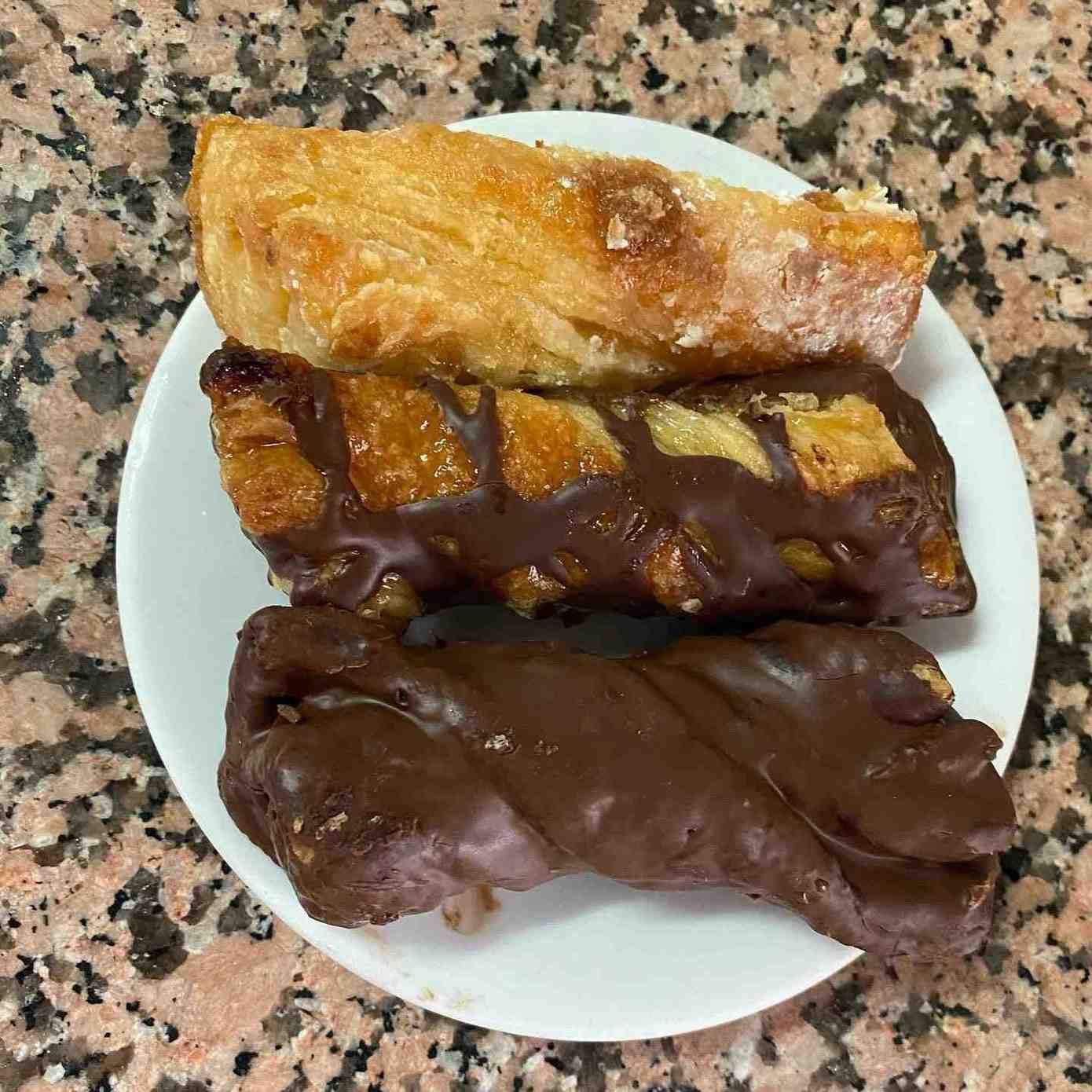 Tres pasteles bañados en chocolate sobre un plato blanco en una encimera de granito.