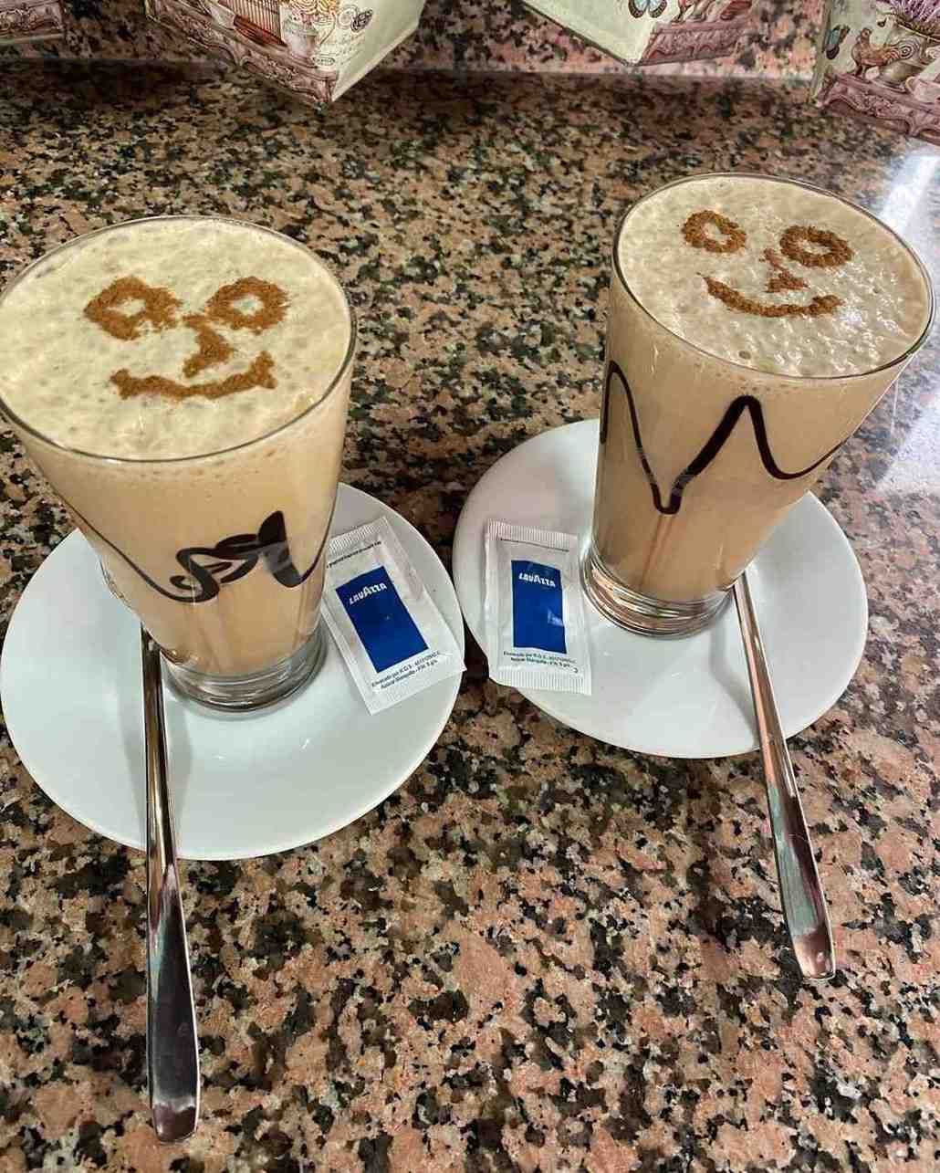 Dos bebidas de café helado con forma de sonrisa, servidas en platillos con cucharas, sobre una encimera moteada.