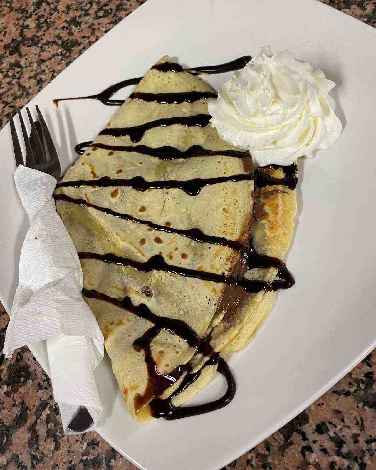 Crepe en un plato blanco, rociado con chocolate y cubierto con crema batida.