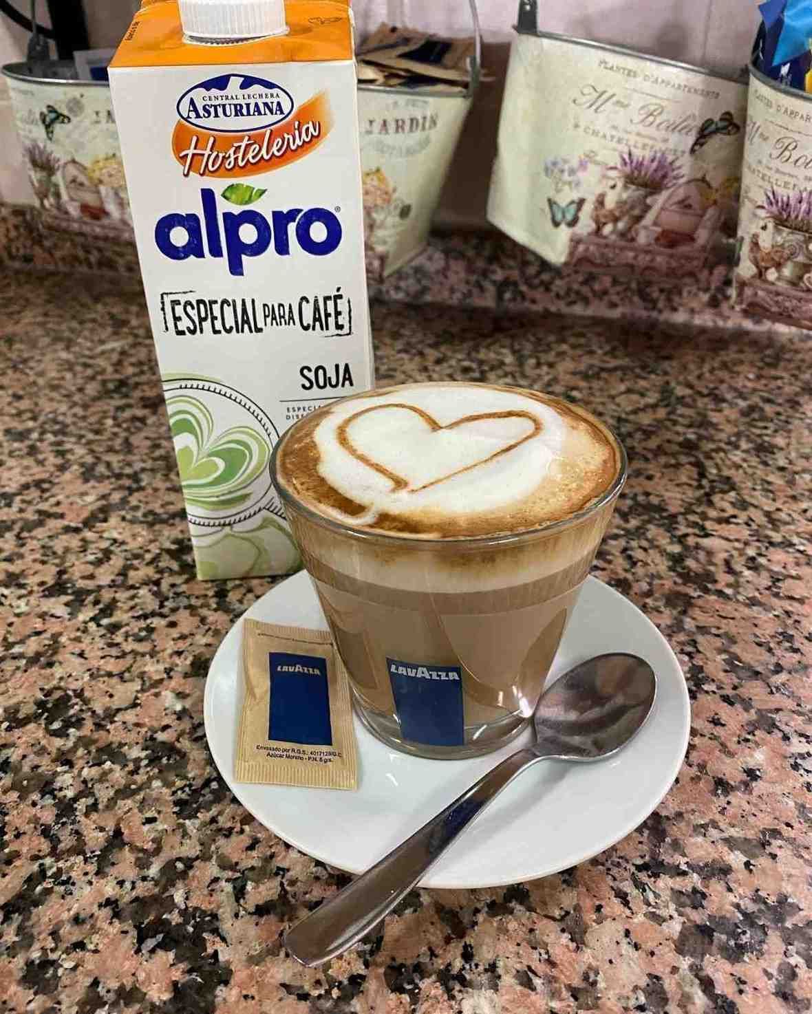 Café con arte latte acompañado de leche de soja Alpro y una galleta en un platillo.