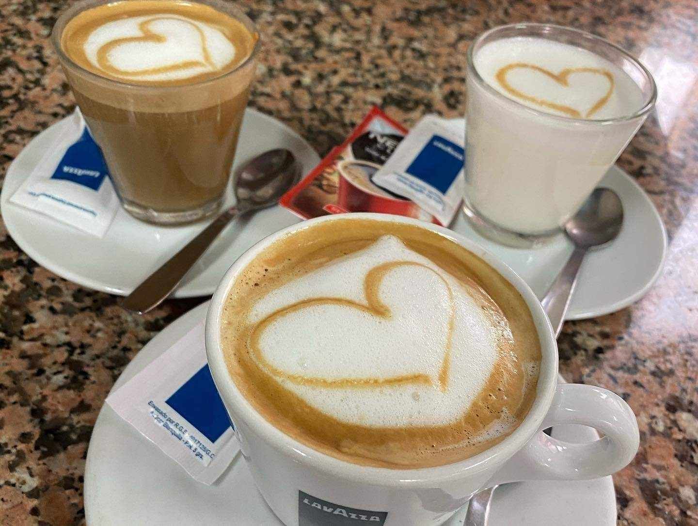 Tres tazas de café con dibujos de corazones en los platillos, sobre una mesa de café moteada.