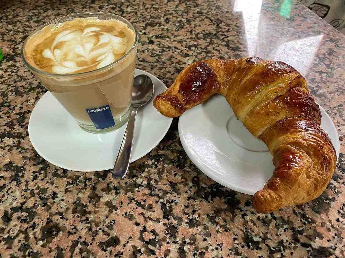 Café y cruasán en platillos blancos sobre una mesa de granito de una cafetería.