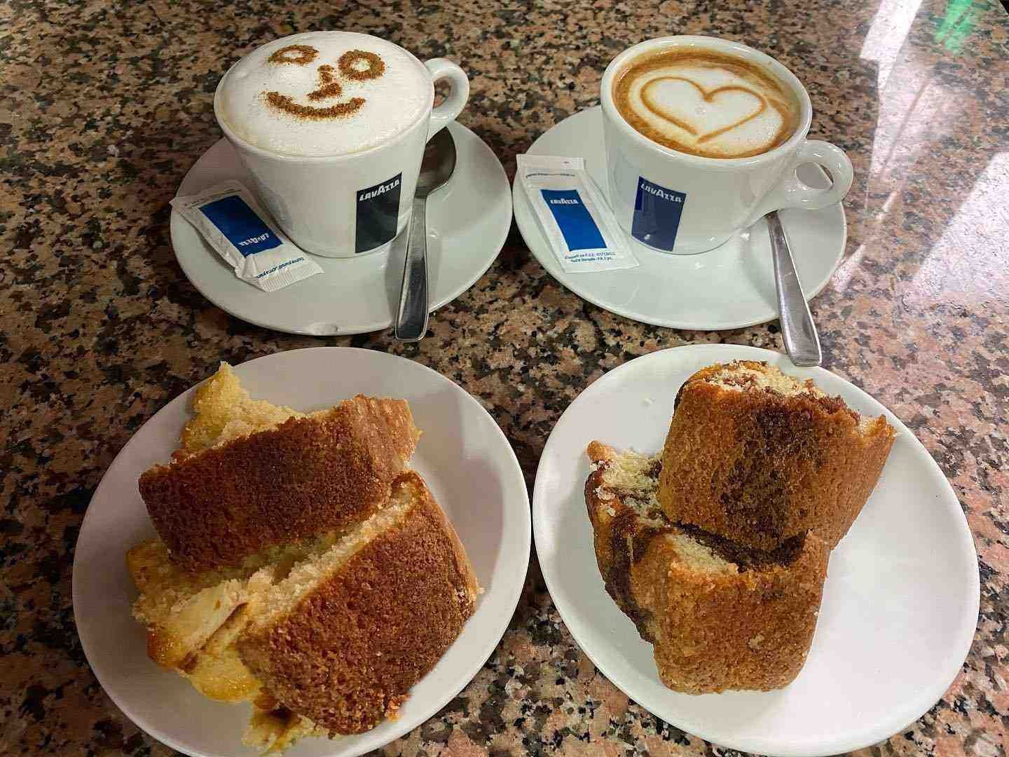 Dos capuchinos con arte latte y dos platos de sándwiches tostados en una mesa.