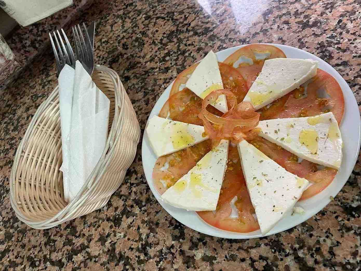 Plato de pizza o pan plano en porciones sobre una mesa de granito, junto a una cesta con tenedores y servilletas.