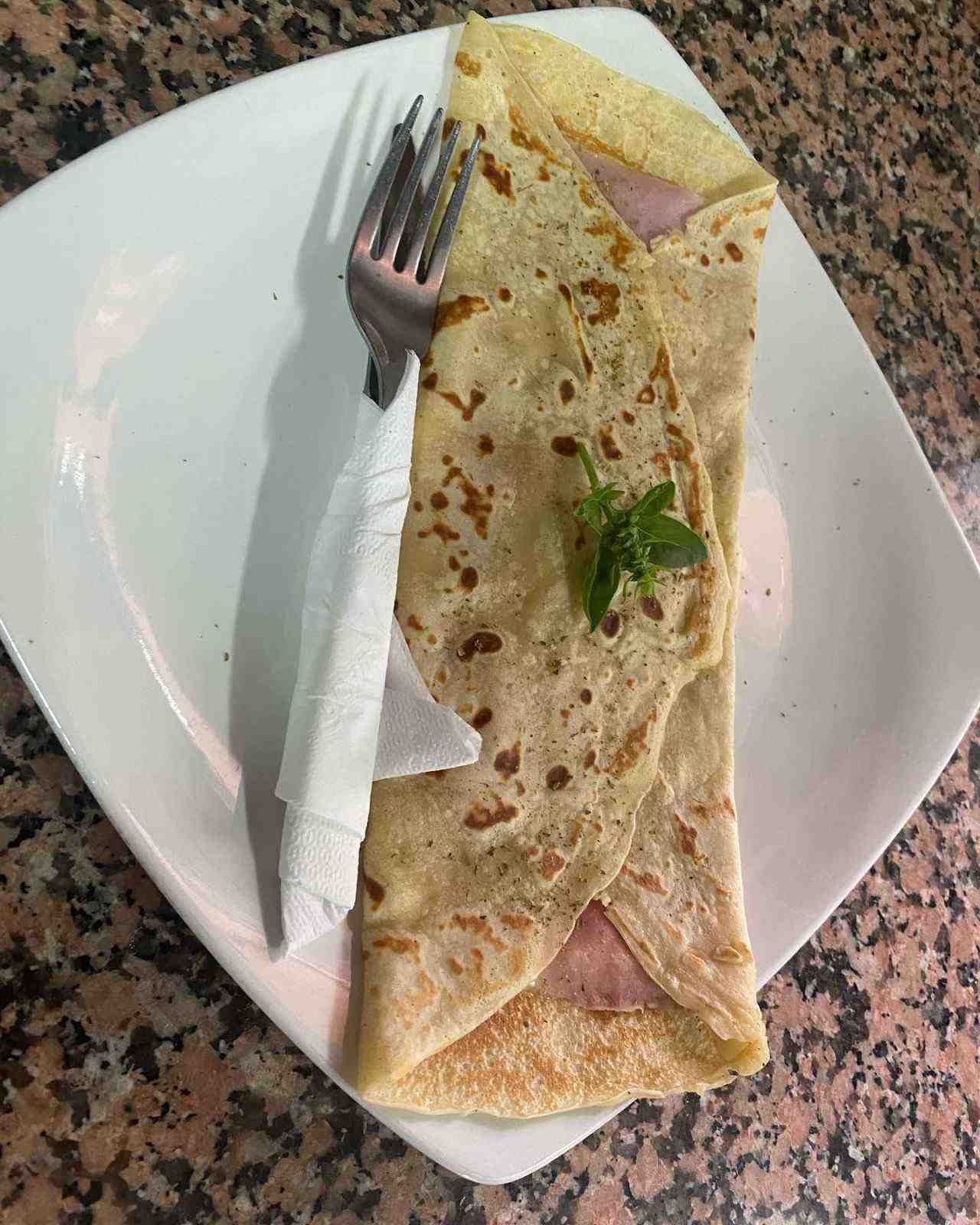 Crepe doblada sobre un plato blanco con tenedor y servilleta sobre una mesa de granito.