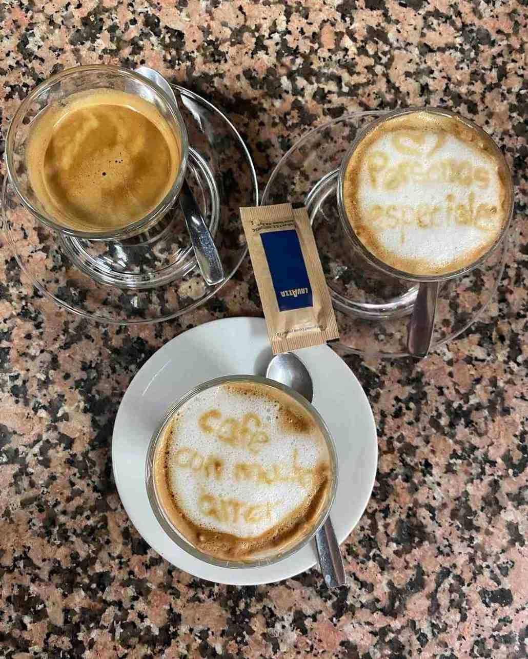 Tres capuchinos sobre una mesa de granito, cada uno con dibujos hechos con café en la espuma.